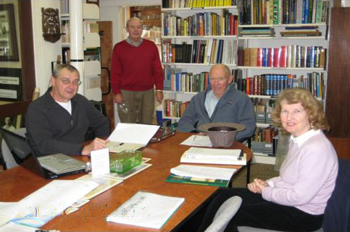 3 people sitting and 1 standing around table with open books